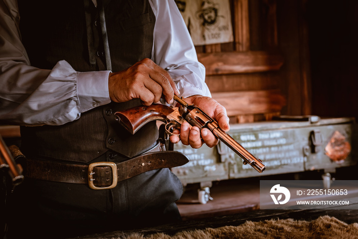 Closed up cowboy loading bullets into gun on hand before used to shot , vintage style.