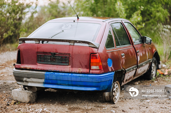 An old, beautiful red wrecked after an accident, discarded car stands in a landfill with punctured wheels after the war in Ukraine.