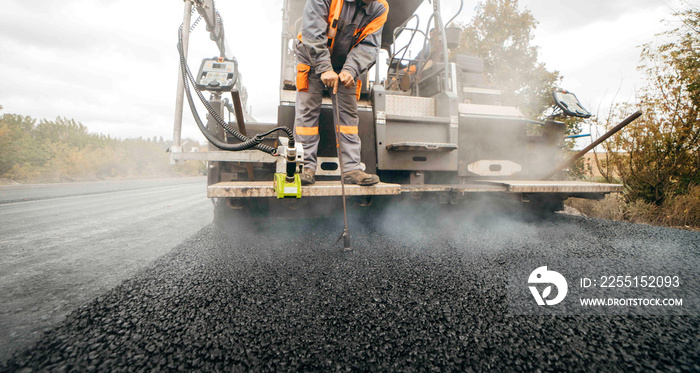 Road service build the highway, road worker measures the depth of fresh asphalt