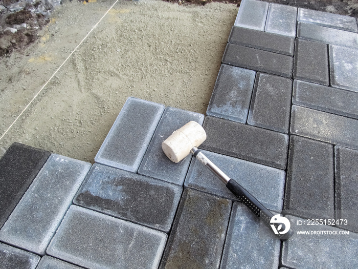 A white rubber mallet lies on the surface of a gray Brick paving slab. Tools and materials for paving works. Beautiful building background with copy space