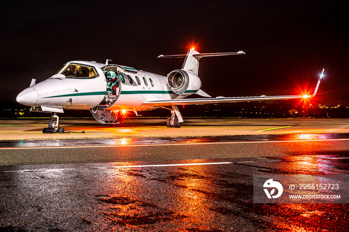 A business jet at night parked on wet apron with position lights illuminated waiting for passengers.