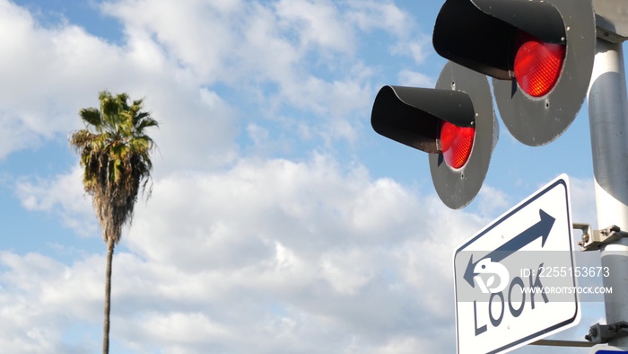 Level crossing warning signal in USA. Crossbuck notice and red traffic light on rail road intersection in California. Railway transportation safety symbol. Caution sign about hazard and train track