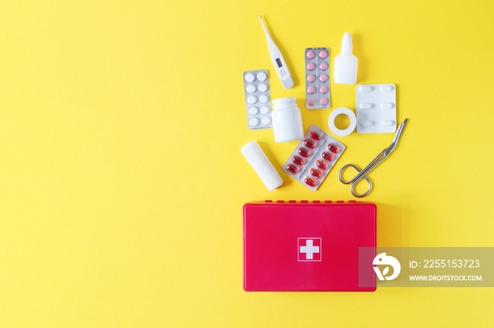 First aid kit red box with medical equipment and medications for emergency top view on pastel yellow background.