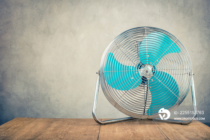 Retro old portable office or home cooling fan standing on desk front concrete wall background. Vintage instagram style filtered photo