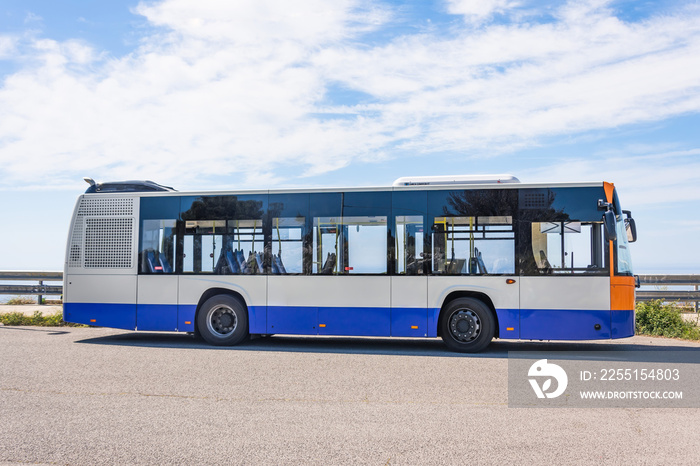 City bus on the side of the road stop, side view on sky background.