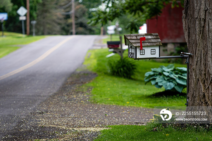 a traditional American wooden mailbox that looks like a cottage, on the side of a village road