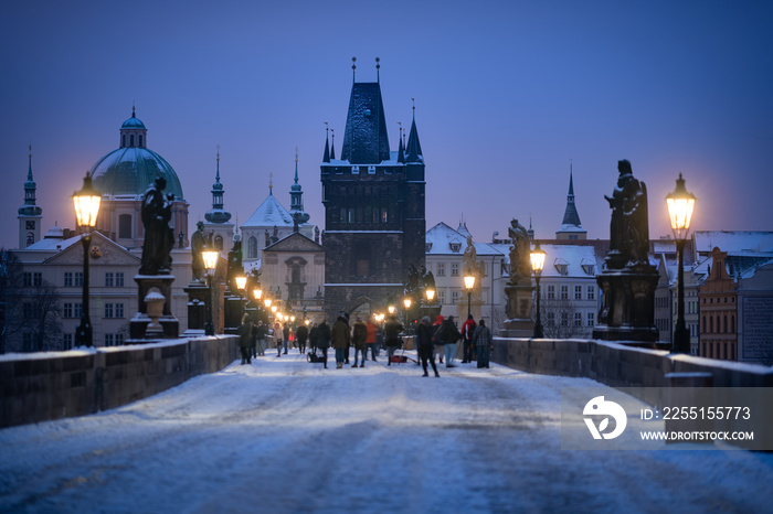 The Old Town Bridge Tower with the famous Charles Bridge, Prague. Atmosphere of winter blue hour before sunrise, with blurred tourists in the foreground.