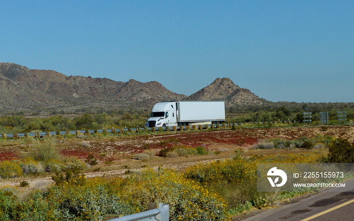 White big rig American long haul semi truck with moving on wide divided turning highway with mountain