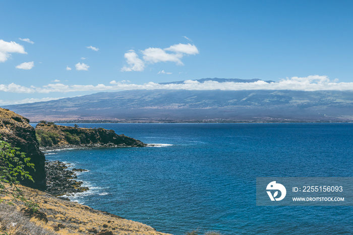 A high angle sweeping view of Maui Hawaii at mid day with a mountain, clouds and the Pacific ocean in the distance