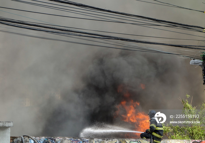 firefighter suppressing flames on the street. black Smoke on background