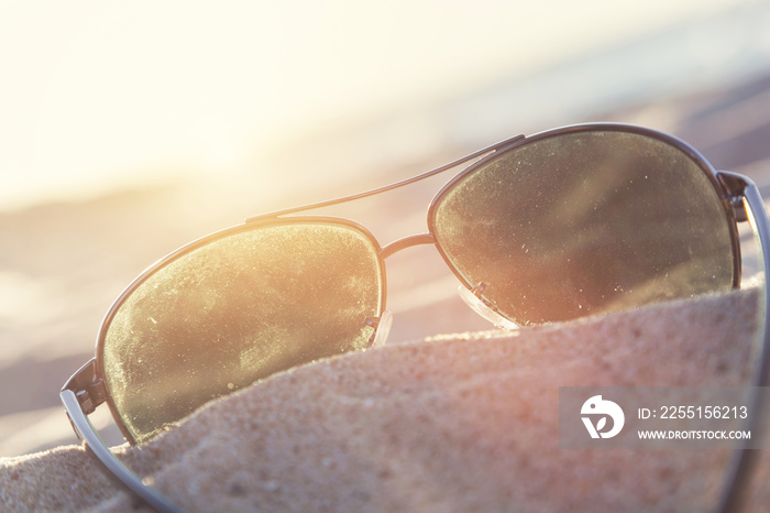 Sunglasses on sand at sunset, beach and ocean in the background.