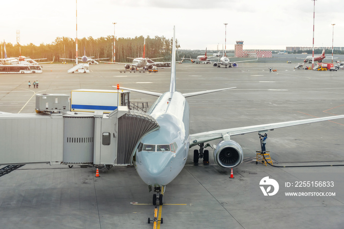 Commercial passenger airplane in the parking at the airport terminal with a nose forward and a gangway. Service and preparation for the flight.