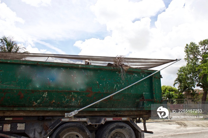 Full roll-off construction dumpster being transported with debris cover, on removal truck