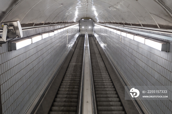 Bright lights leading down super long escalator leading to underground subway station