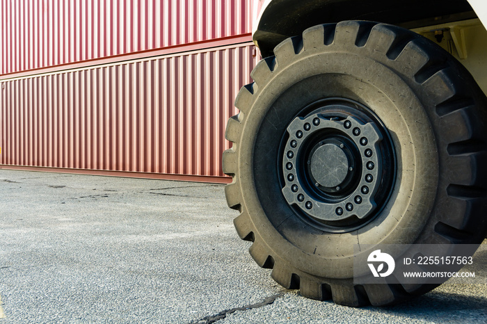 Wheel of a reach stacker and stacked cargo containers in a shipping yard.