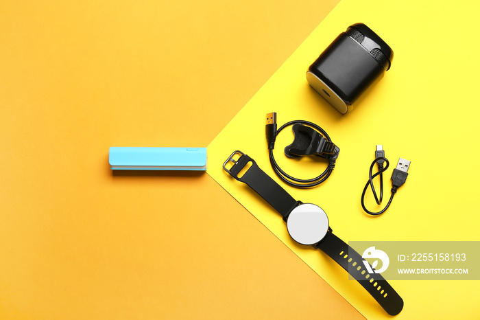 Power bank with USB cable, smartwatch and speaker on color background