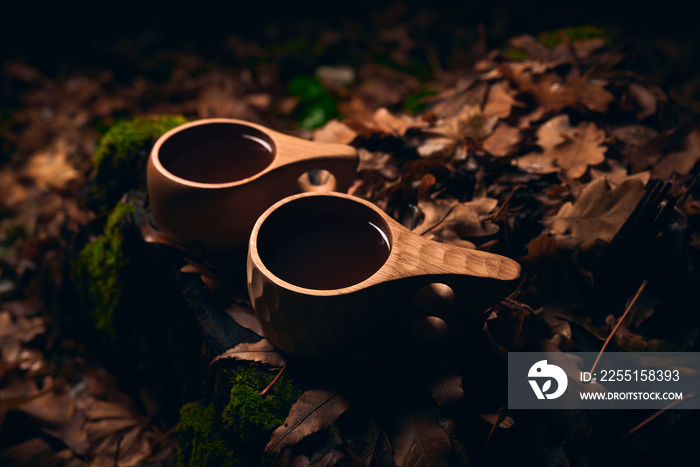 Tea in a two wooden national mugs Kuksa in the autumn forest at night