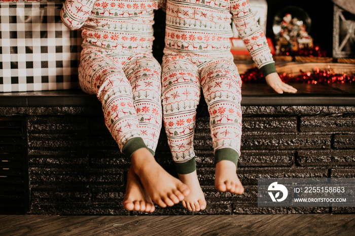 siblings sitting side by side wearing christmas pajamas