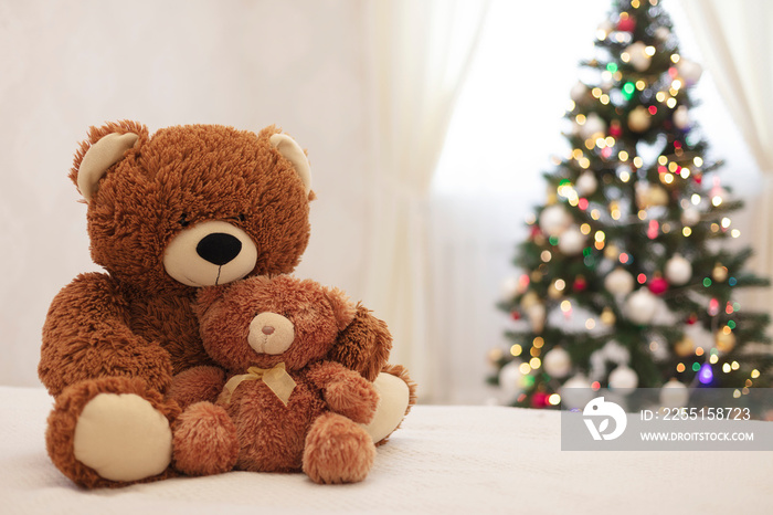 Merry Christmas! Children’s toys teddy bears big and small are sitting on the sofa against the background of the Christmas tree.