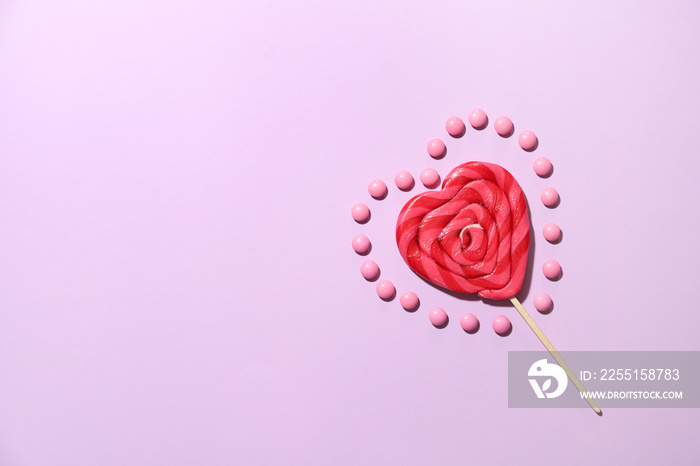 Lollipop in shape of heart and candies on color background