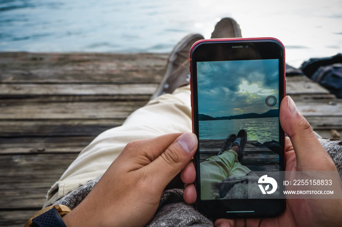 Man hands taking a picture of the sunset, he is lying on the shore of a lake