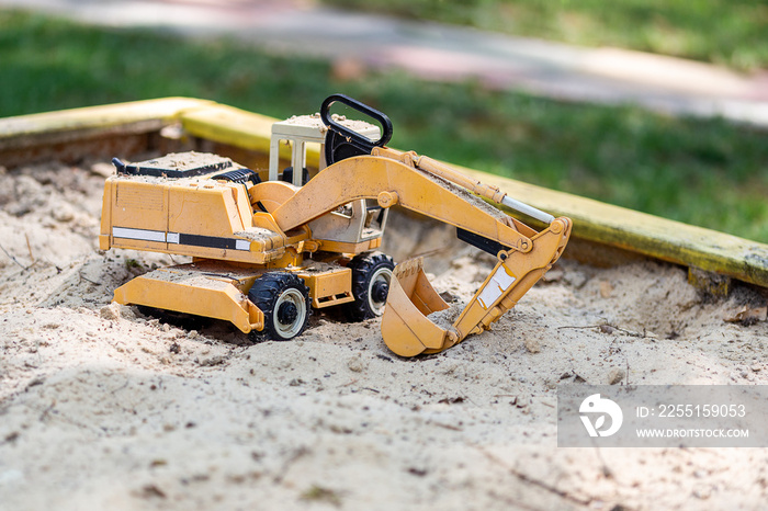 Yellow excavator toy in wooden sandbox at yard. Boy’s toys concept