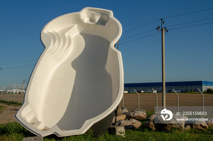 An exhibition sample advertising a large fiberglass white swimming pool. Against the background of stones and the blue sky. A large swimming pool is a sample. Promo pool offer. A photo from the front.