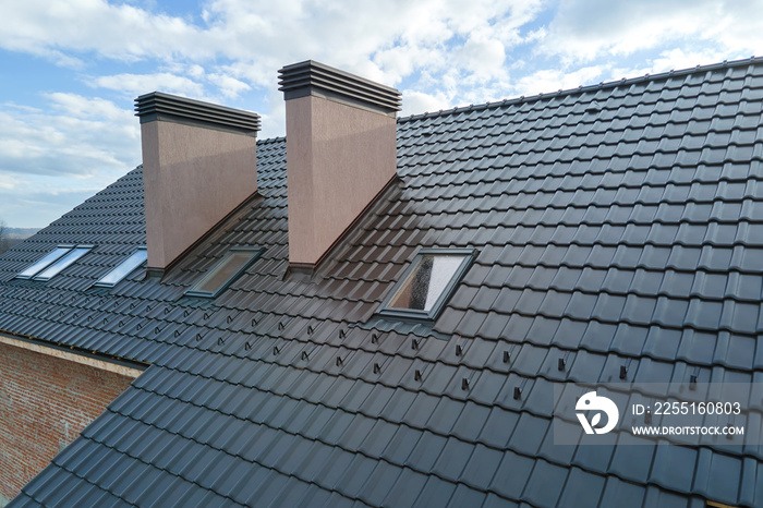 Closeup of attic windows and brick chimneys on house roof top covered with ceramic shingles. Tiled covering of building