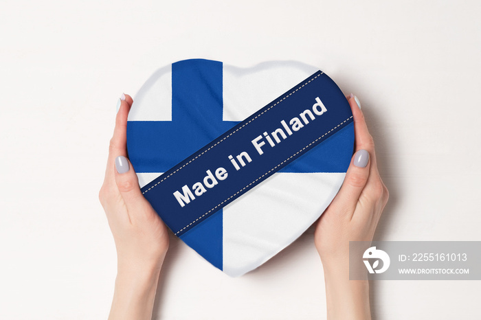 Inscription Made in Finland the flag of Finland. Female hands holding a heart shaped box. White background.