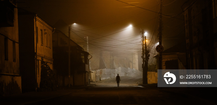 Lonely woman walking in foggy old city with street lights in a coat