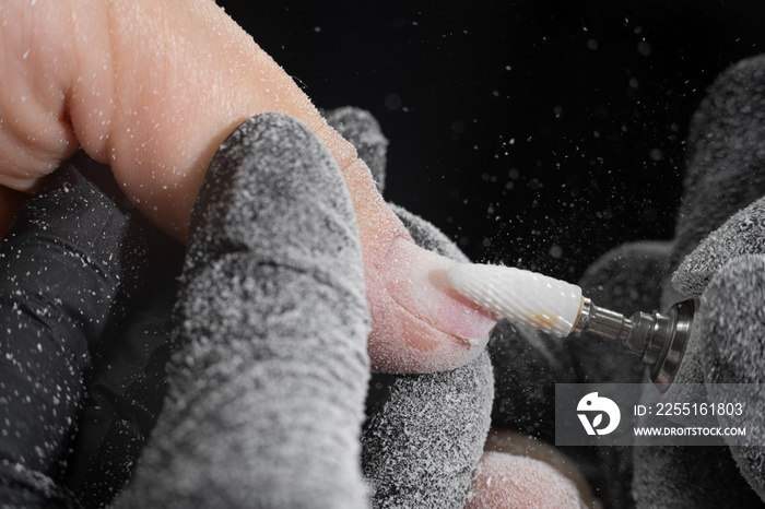 Closeup shot of master in rubber gloves applying an electric nail file drill to remove the nail polish in the beauty salon. Perfect nails manicure process with flying dust or debris