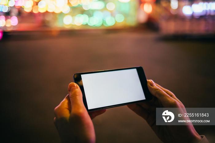 Mobile phone with blank screen in woman’s hand on background festively lit