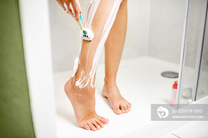 Woman shaving her legs with razor and foam in the shower cabin