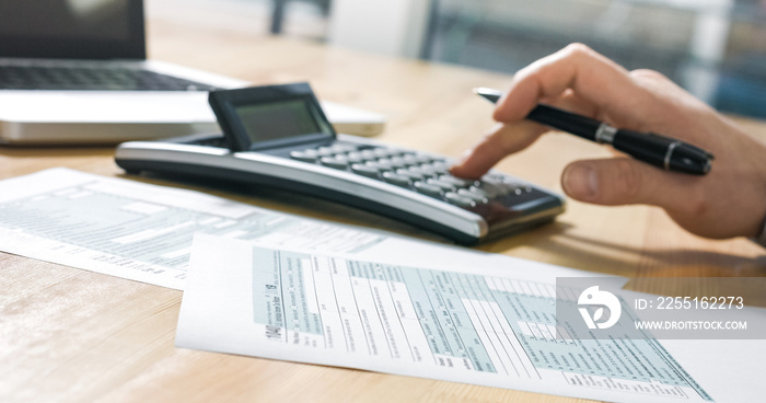 Closeup of US tax form 1040 and businessman hand calculating and filling report paper at the office.