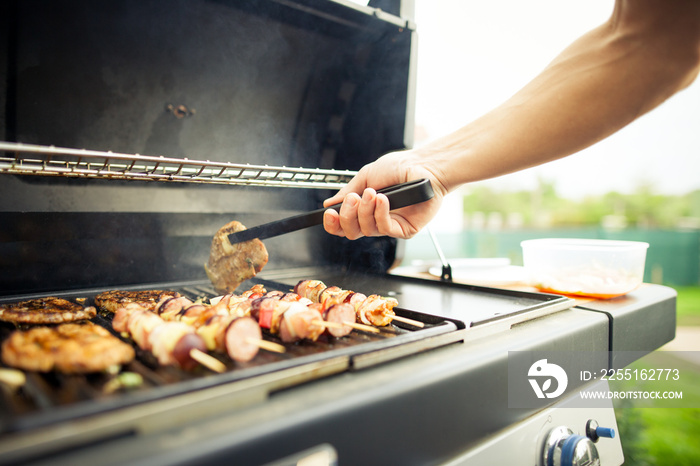 Young man hands turning the meat by fork on the gas grill (color toned image)