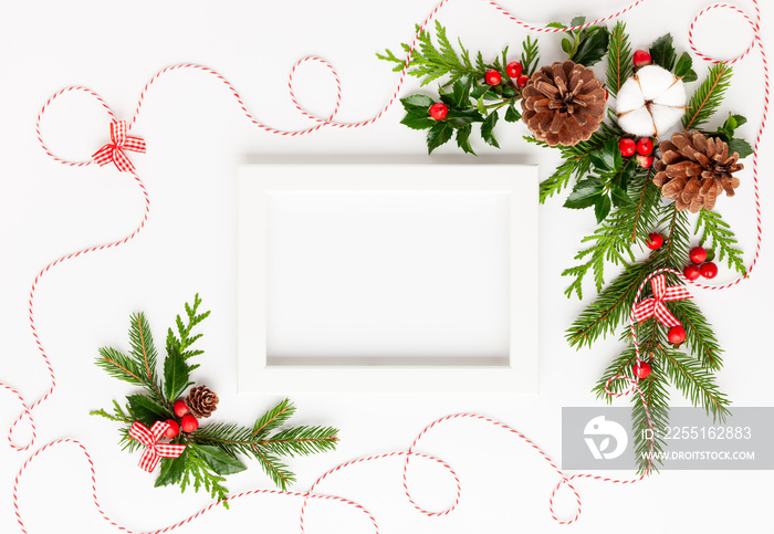 Christmas composition  with photo frame, cotton flower, branches of spruce and holly with red berries on white background. Merry christmas greeting card with empty space for holiday text.