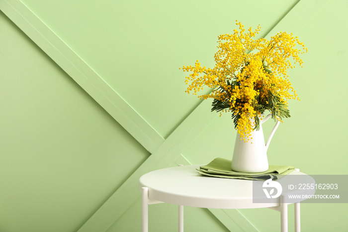 Vase with beautiful mimosa branches on table near color wall in room