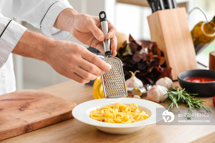 Male chef grating garlic into plate with pasta in kitchen, closeup