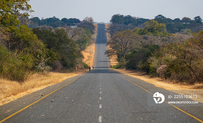 African straight road with unrecognizable people walking