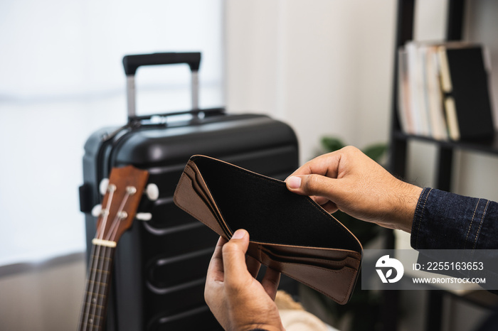 Close up male traveller hand open the empty wallet near trolley bag in the house.There is no money in wallet. No budget to travel