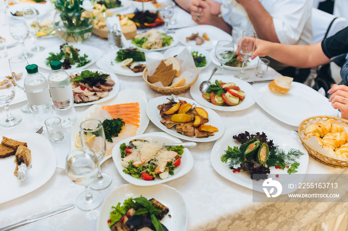 People are sitting at a table with a white tablecloth surrounded by plates of different foods. Lunch at the restaurant.