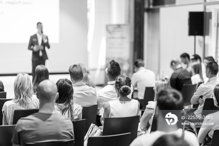 Speaker giving a talk in conference hall at business event. Focus on unrecognizable people in audience. Business and Entrepreneurship concept. Black and white image.