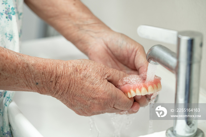 Asian senior or elderly old woman patient holding and washing denture in nursing hospital ward; healthy strong medical concept