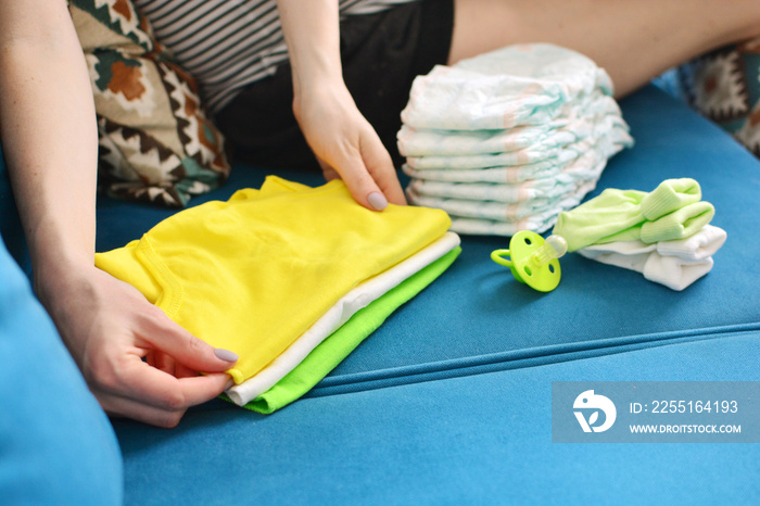 Pregnant woman packing bag for maternity hospital at home. Expectant mother folds clothes for a newborn.