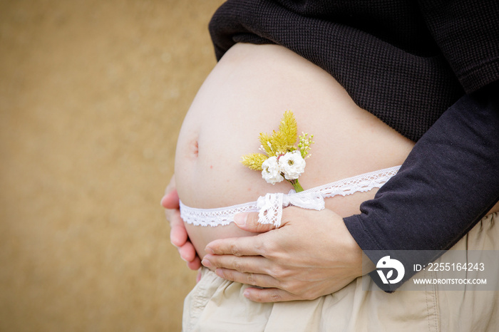 リボンを巻いて小さな花を添えた妊婦さんのお腹クローズアップ