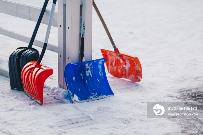 Colourful four plastic shovels stand on snow. Winter time. Shoveling deep snow. Season and cleaning concept. Removal spades near hence on ground covered with snow