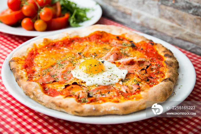 Pizza with egg in the middle. Neapolitan pizza with tomato sauce, cheese and ham. Authentic Italian recipe.