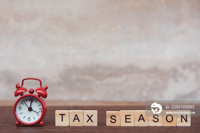 Tax season with wooden alphabet blocks and Red alarm clock, on Table dark plank wooden background with copy space