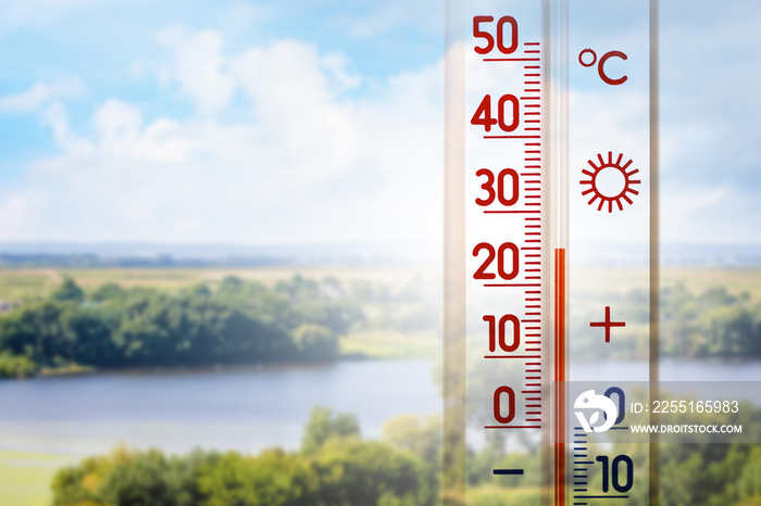 The thermometer on a background of summer landscape in sunny weather shows 25 degrees heat_