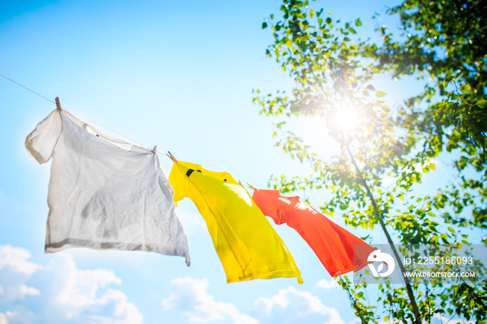 Photo of three T-shirts hanging on rope on background of blue sky with treetops.